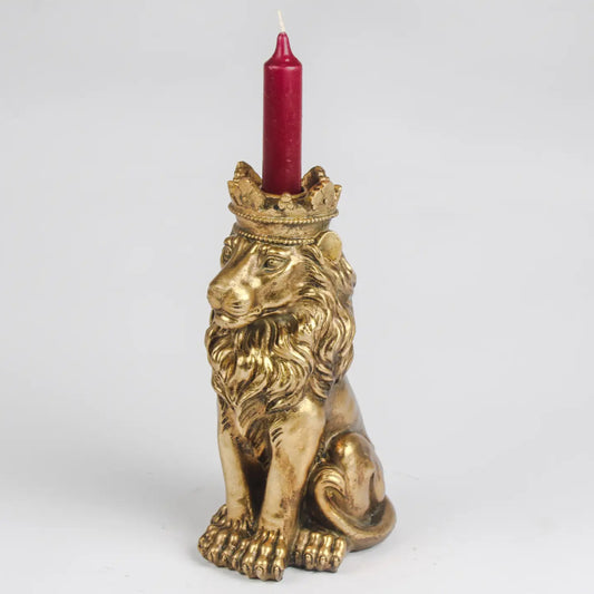 A gold-toned lion figurine candle holder with a crown on its head, holding a red taper candle, photographed against a light gray studio background.