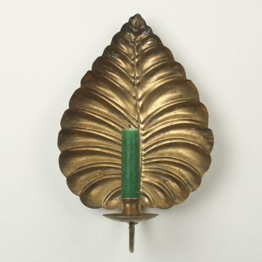 A vintage-style brass leaf-shaped wall sconce holder with a green candle inserted in the center, set against a plain off-white background.