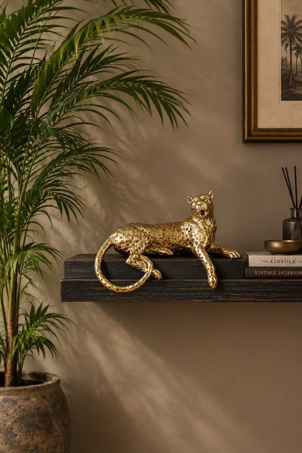 A metallic gold leopard figurine resting on a dark wooden floating shelf in a styled interior setting with a potted palm plant, a framed print, and decorative books.