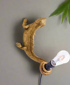 Gold lizard-shaped wall lamp with a light bulb on a white background