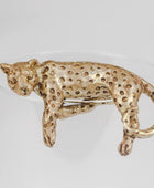 A leopard-shaped brooch in textured gold-tone metal with a spotted pattern, shown on a plain light gray background.