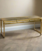 Gold metal bench against a plain wall on a wooden floor