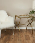 Gold side table with glass top next to a white fur chair on a wooden floor.