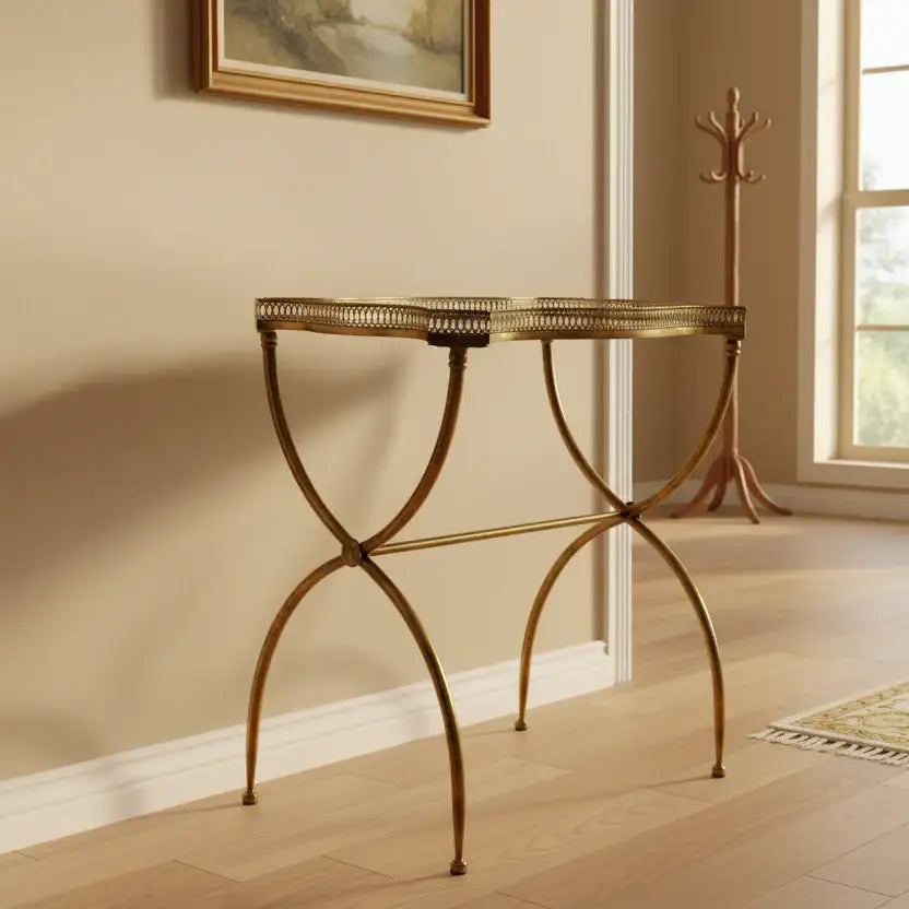 Gold metal side table in a room with a coat rack and painting on the wall.