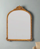 Decorative gold-framed mirror on a gray wall with a beige chair partially visible.