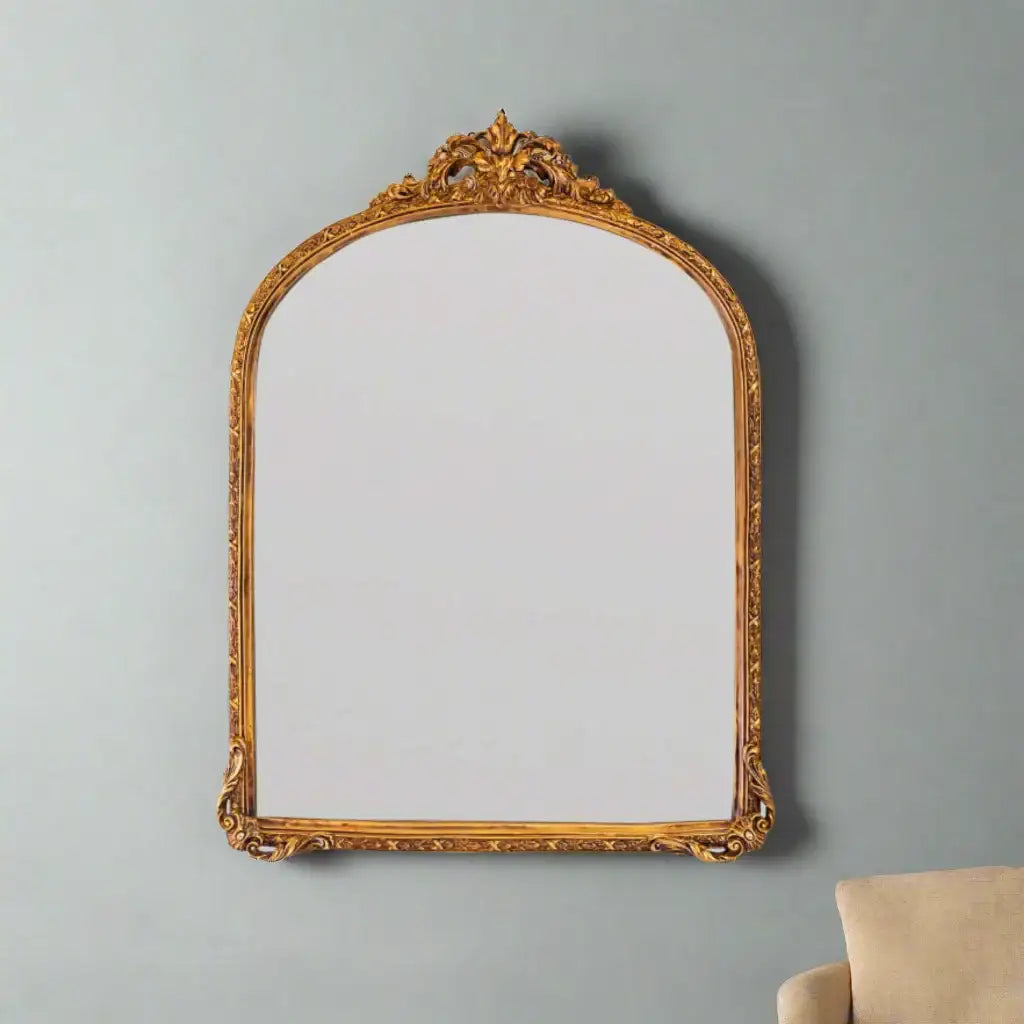 Decorative gold-framed mirror on a gray wall with a beige chair partially visible.