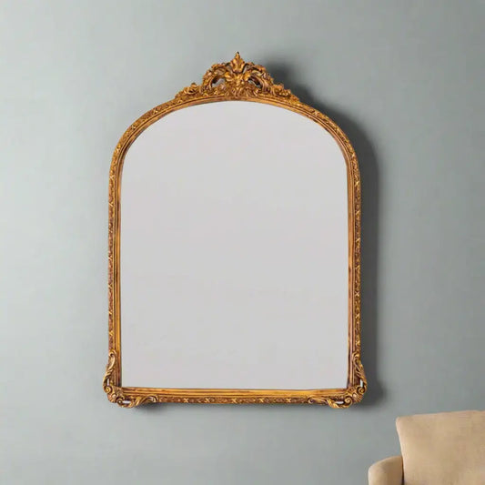 Decorative gold-framed mirror on a gray wall with a beige chair partially visible.