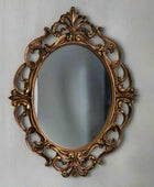 Decorative oval mirror with intricate gold frame on a light gray wall