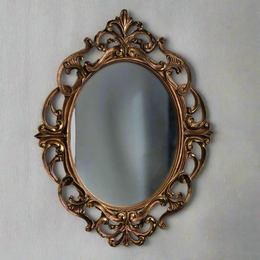 Decorative oval mirror with intricate gold frame on a light gray wall