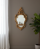 Decorative gold mirror on a gray wall with a plant and white curtain.