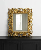 Decorative gold mirror with intricate patterns on a black cabinet against a white wall