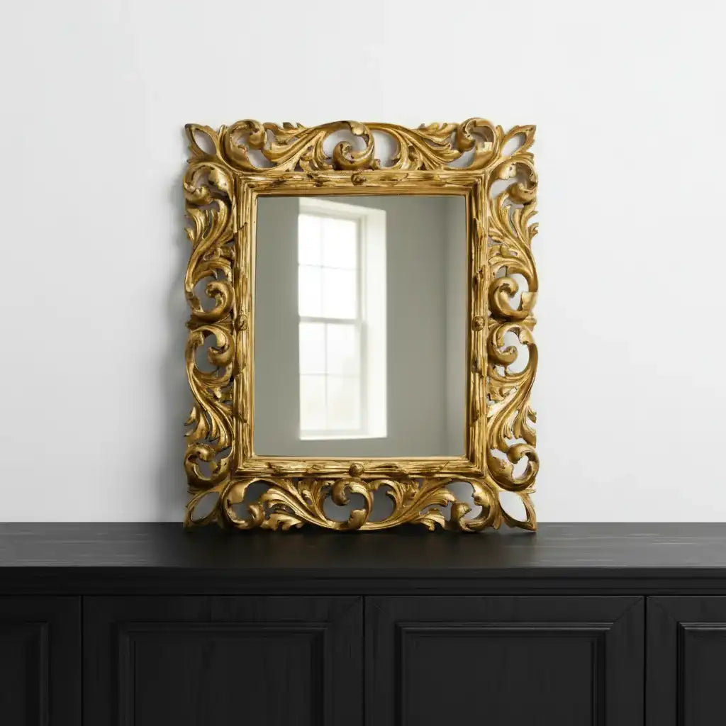 Decorative gold mirror with intricate patterns on a black cabinet against a white wall