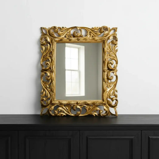 Decorative gold mirror with intricate patterns on a black cabinet against a white wall