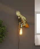 Gold parrot-shaped wall light fixture with a lit bulb on a brown wall.