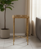 Gold side table in a living room setting with a plant and sofa.