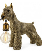 A decorative table lamp shaped like a Scottish Terrier dog, holding a clear light bulb in its mouth. The dog figure has a textured brown and gray coat with gold-toned ears and muzzle details, and the bulb socket has a brass-colored metal cap.