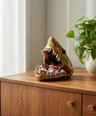 Decorative candy dish shaped like a shark on a wooden surface with a plant in the background