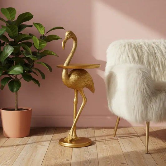 Gold flamingo-shaped side table in a room with a pink wall, plant, and white chair.