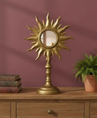 Decorative sun-shaped mirror on a wooden surface with books and a plant against a purple wall.
