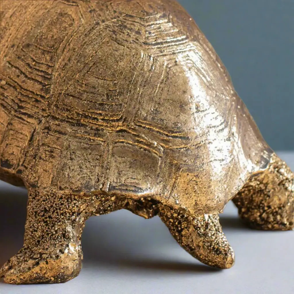 Close-up of a bronze turtle sculpture on a neutral background
