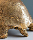 Close-up of a bronze turtle sculpture on a neutral background