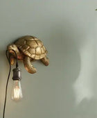 Gold turtle-shaped wall light fixture with a bulb on a neutral background