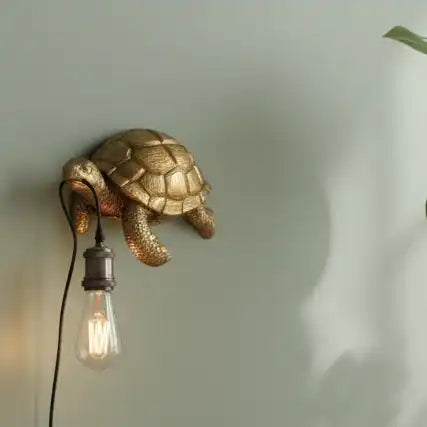 Gold turtle-shaped wall light fixture with a bulb on a neutral background