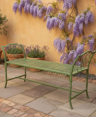 Green metal bench in a garden setting with wisteria and potted plants.