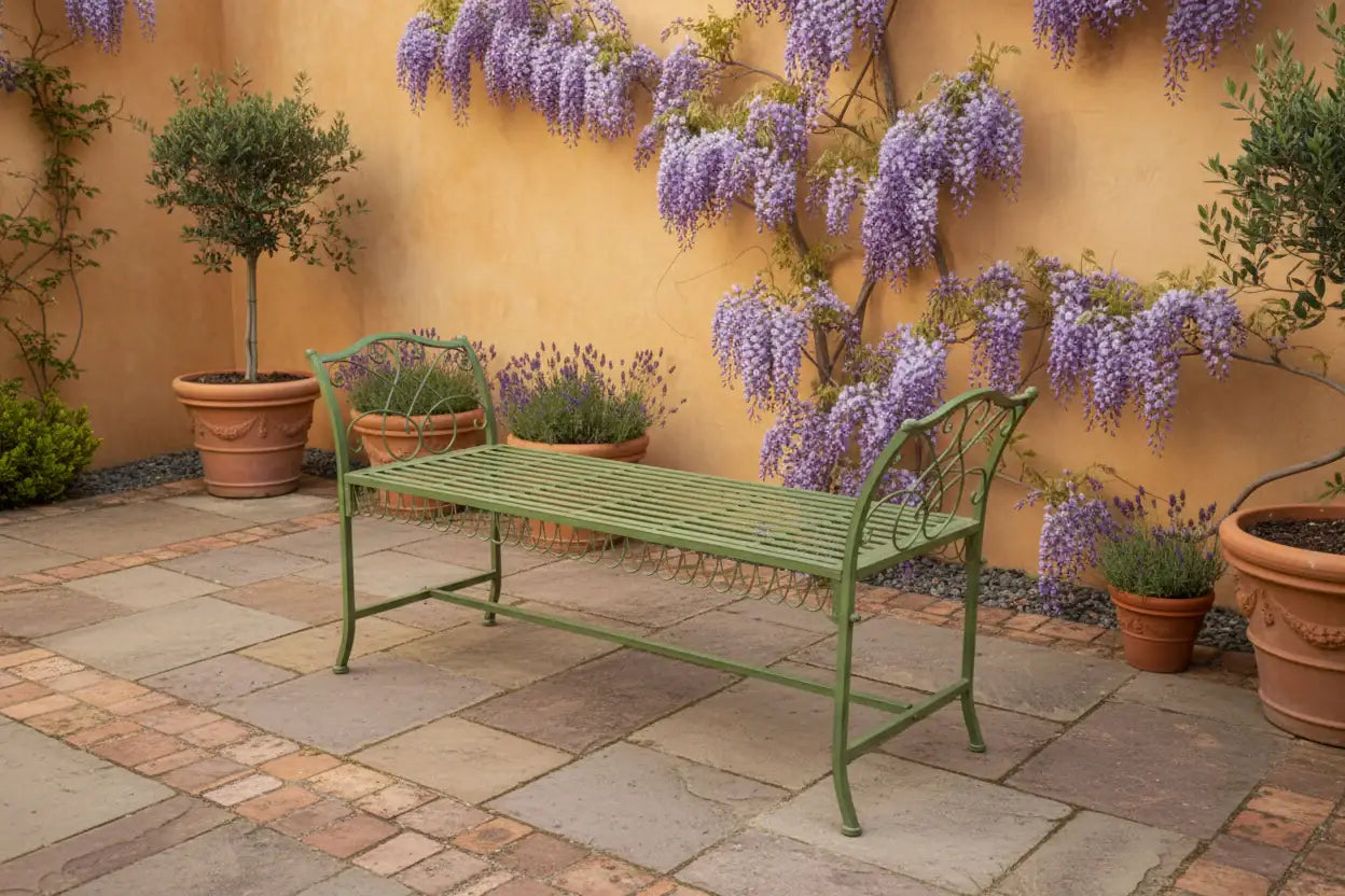 Green metal bench in a garden setting with wisteria and potted plants.