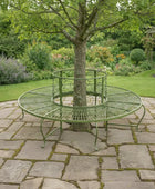 Round metal garden seat wrapped around a tree in a lush garden setting