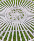 Decorative white metal table with intricate design on a grassy background
