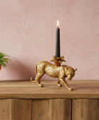 Gold panther candle holder with a lit black candle on a wooden surface against a pink wall.
