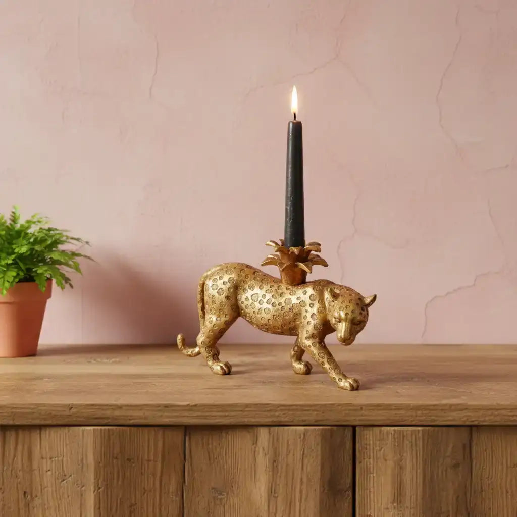 Gold panther candle holder with a lit black candle on a wooden surface against a pink wall.