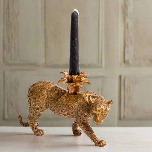 Gold panther candle holder with a black candle on a neutral background