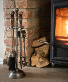Set of metal fireplace tools next to a lit wood stove with logs in front of a brick wall.