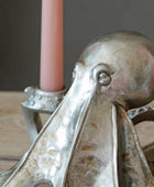 A close-up of a metallic octopus-shaped candle holder with a pink candle inserted, set on a wooden surface against a dark gray background.