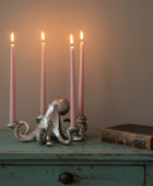 A silver octopus-shaped candle holder with four slim pink taper candles, displayed on a wooden surface against a neutral beige background.