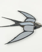 A swallow-shaped brooch or pin with mirrored gray wings and a dark metallic body, shown on a plain light background.