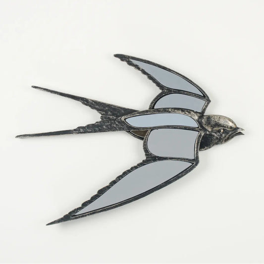 A swallow-shaped brooch or pin with mirrored gray wings and a dark metallic body, shown on a plain light background.