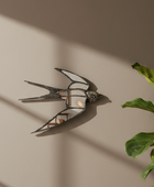 A decorative wall mirror shaped like a swallow, mounted on a beige wall. The mirror has a dark, textured frame and reflects a miniature living room scene.