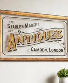Vintage-style sign for 'The Stables Market Antiques, Camden, London' on a wall with decorative items below.