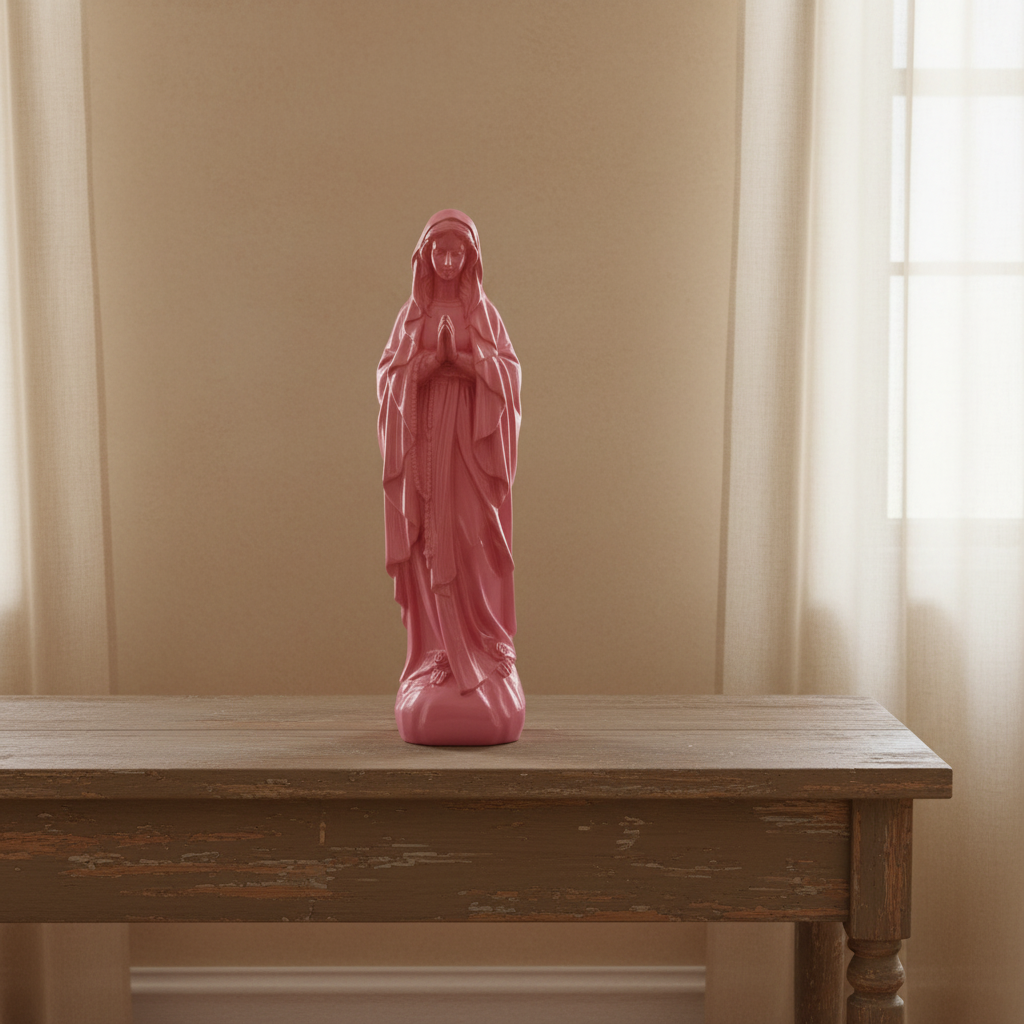 A pink religious figurine of the Virgin Mary standing on a rustic wooden table against a beige wall with sheer curtains.