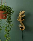 Decorative gold lizard wall light fixture next to a hanging plant on a green wall.