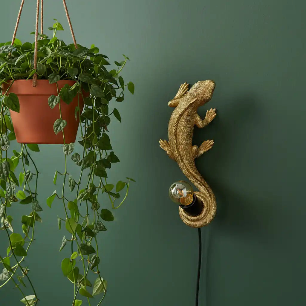 Decorative gold lizard wall light fixture next to a hanging plant on a green wall.