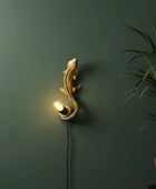 Decorative wall light shaped like a lizard on a green wall with a plant.