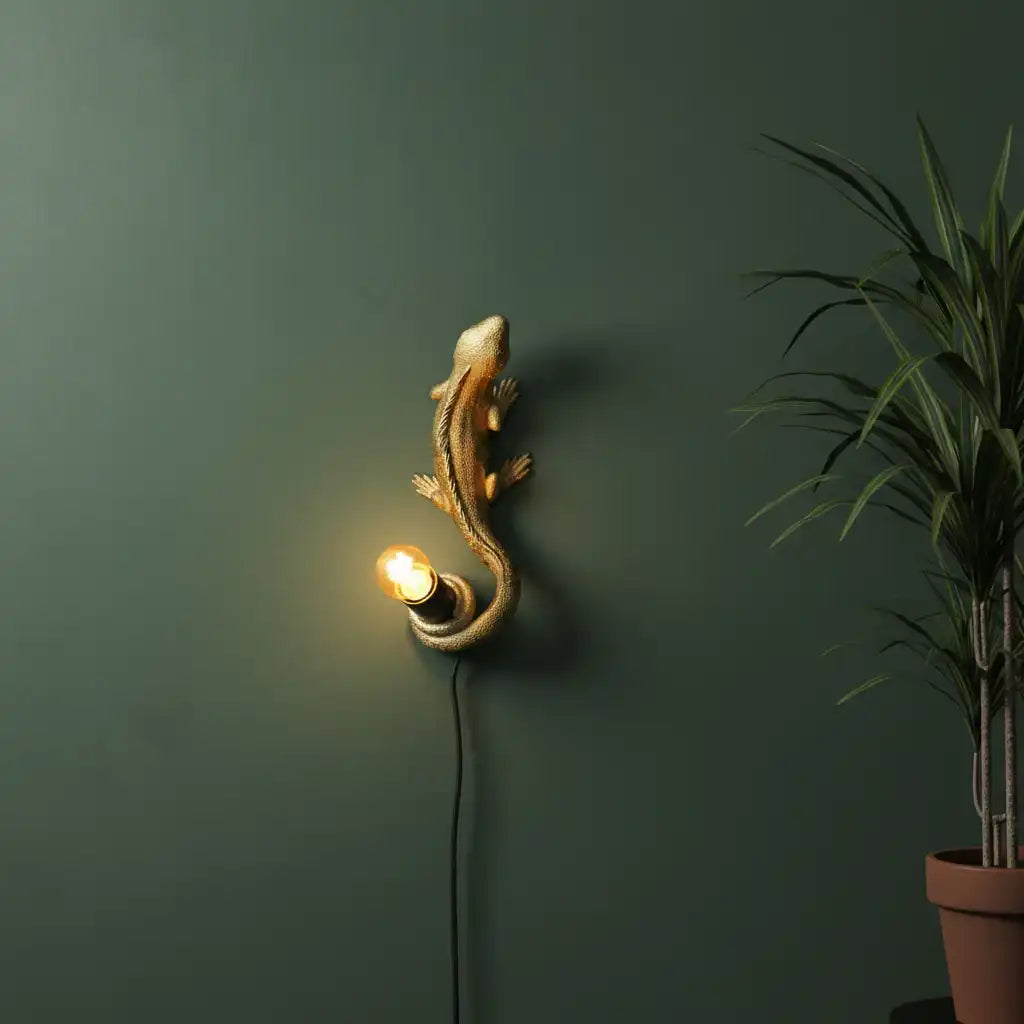 Decorative wall light shaped like a lizard on a green wall with a plant.
