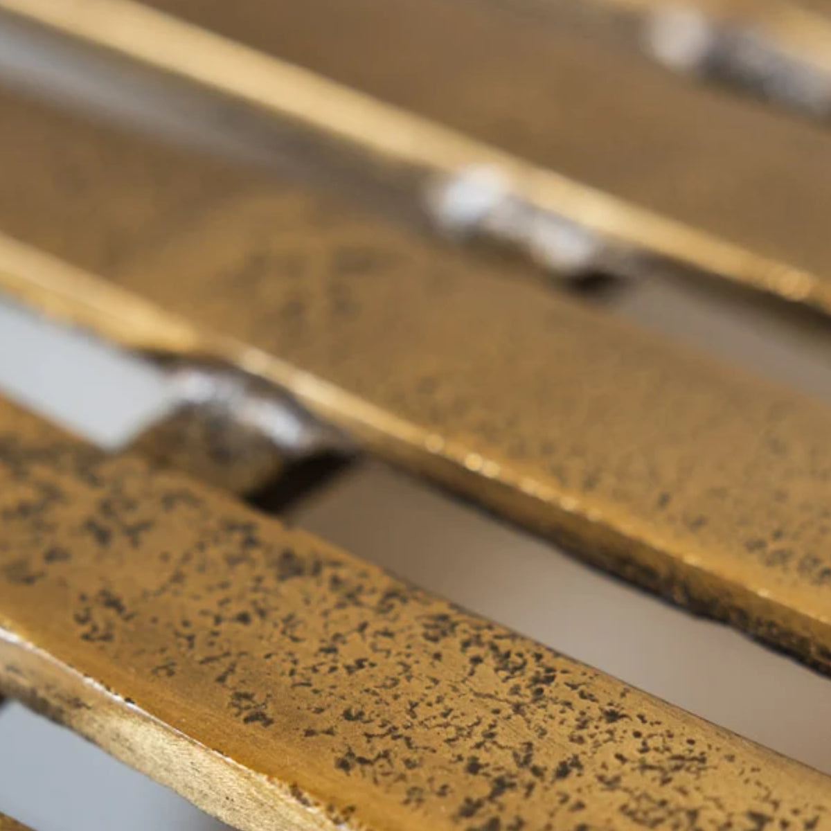 Close-up of a distressed gold metal slatted surface, showing a textured, speckled finish with warm metallic tones.