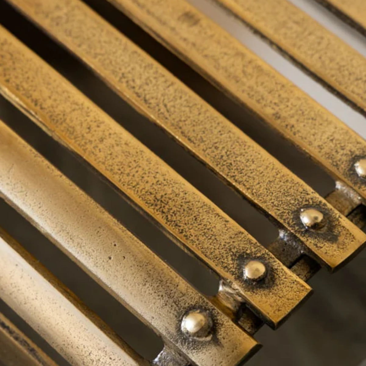 Close-up of a brass radiator fin with vertical slats and decorative rivets, showing a textured antique gold finish.