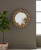 Decorative mirror with leaf pattern on a gray wall next to a potted plant.