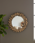 Round decorative mirror with leaf pattern on a wall next to a plant